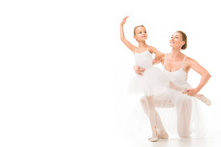 微笑的成年女教练帮助小芭蕾舞者在白色背景下独立锻炼