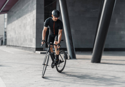 远处的运动运动员骑着专业自行车在现代建筑旁边的城市桥梁。 骑自行车的专业自行车训练日。 积极生活方式和户外爱好的概念。