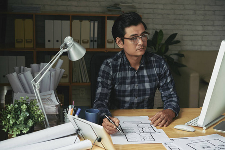 专业的亚洲建筑师用电脑检查桌子上的蓝图