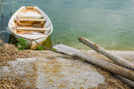 古老的木船，绿色的泥泞的河流。 在旧木桨旁边。 当地和农村景观。 简单而质朴，但生锈的等级停在生锈的混凝土海岸附近。