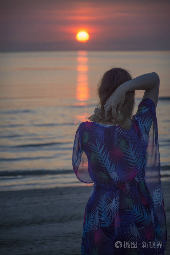 一个女人站在海滩上看着大海里的日出
