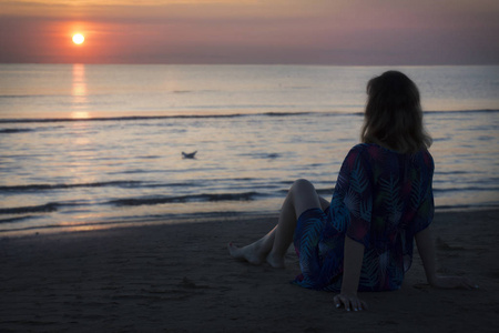 一个女人坐在海滩上看着大海里的日出