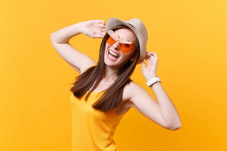 兴奋微笑的年轻女子的肖像，戴着稻草夏帽，橙色眼镜，双手放在头上，看着一边，在黄色的背景上孤立无援。 人们真诚的情感生活方式观念。