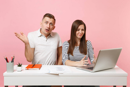两位年轻疲惫的商务女性男性同事坐在白色办公桌前工作，现代笔记本电脑被隔离在粉彩背景上。成就职业概念。复制空间广告，青年合作