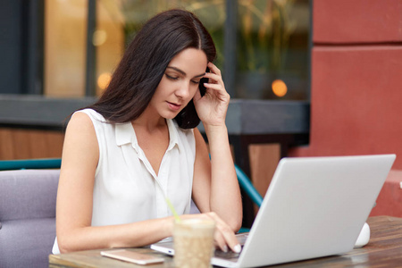 忙碌的女性自由职业者坐在打开的笔记本电脑前,喝咖啡,在新项目上工作