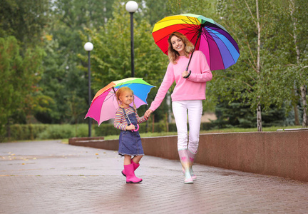 快乐的母女带着明亮的雨伞在公园里散步