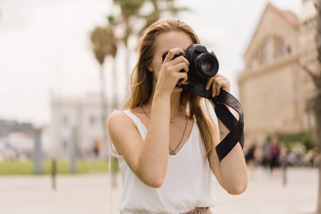 女摄影师，长发，在专业的DSLR相机上拍照，背景是天空草和棕榈树，旅行者在暑假户外拍照。