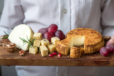 奶酪盘与各种奶酪，葡萄，坚果和手的奶酪制造商在黑色背景。 意大利奶酪和水果盘。