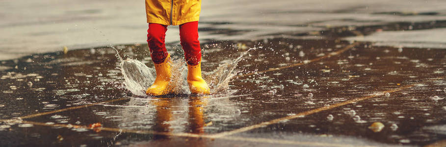 穿着橡胶靴的孩子的腿在秋天的瓦尔斯的水坑里跳