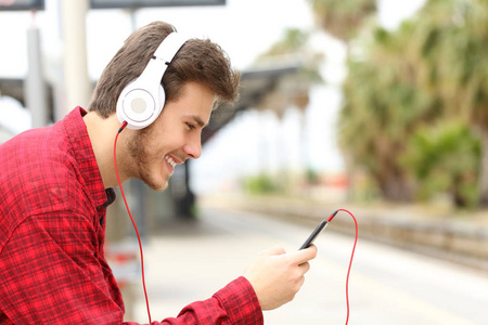 一位在火车站等着手机和耳机听音乐的快乐男人的侧景画像