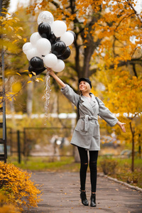 秋天的女人在秋天的公园里拿着气球。 穿灰色外套的时尚女孩