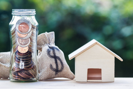 住房贷款抵押贷款，财产投资，储蓄货币概念美元在一个钱袋和罐子小住宅模型在桌子上与自然背景。 交换资金和房屋。