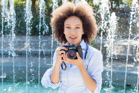 有着复古相机的迷人黑人女性肖像，女摄影师，户外女摄影师，发型，穿着休闲服装，看着相机。