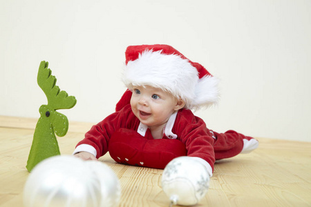 可爱的小宝宝穿着红色圣诞老人服装，躺在地板上玩白色的鲍布