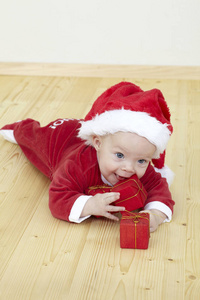 穿着红色圣诞老人服装躺在地上玩礼盒的可爱小宝宝