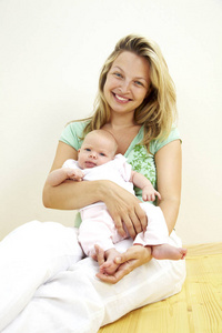 年轻微笑的母亲抱着七个月大的女儿，坐在木地板上