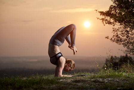 强壮的肌肉，灵活的光脚女人在训练装备上做困难的复杂瑜伽练习户外复制空间背景的浅粉色夏季早晨的天空。健身美容理念..