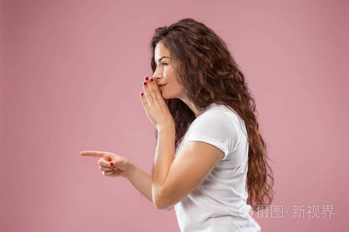 年轻女子在她的手背后耳语一个秘密粉红色背景照片-正版商用图片1304