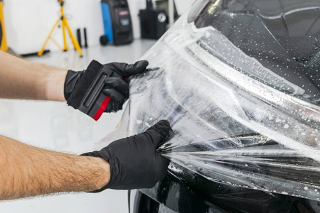 汽车包装专家把乙烯基箔或薄膜放在汽车上。 保护膜。 使用带有工具的保护膜进行工作。 汽车细节。 透明薄膜。 汽车油漆保护。 修剪