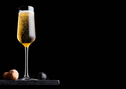 优雅的黄色香槟杯，软木塞和铁丝笼在黑色大理石上的黑色背景。