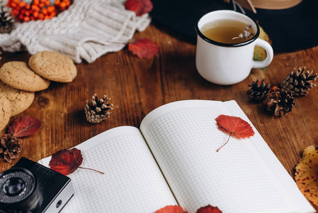 平躺的秋叶和格子纹理毛衣在木制背景与杯茶。 秋天或冬天的概念。