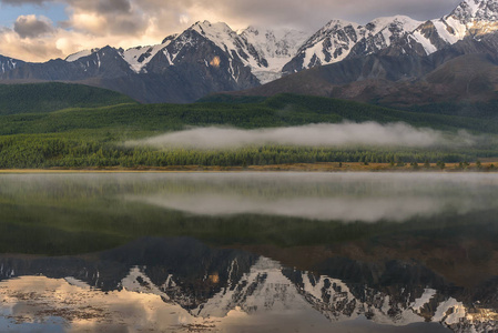 神奇的镜子反射的群山覆盖着雪和绿色的森林，美丽的薄雾在黎明的湖水中