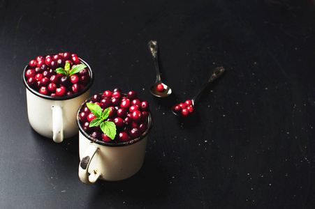 新鲜的红色蔓越莓，薄荷叶在白色的杯子和勺子在黑暗的黑色背景与复制空间。 浆果节日圣诞节背景