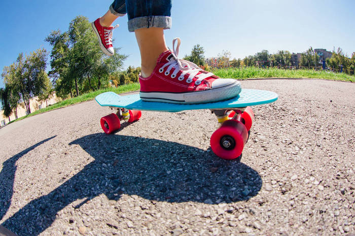 一个穿着红色运动鞋的女孩在带粉红色轮子的蓝色塑料便士滑板上骑着脚