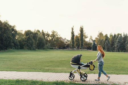 一位年轻的母亲在公园散步，她的孩子在他的婴儿手推车里放松。