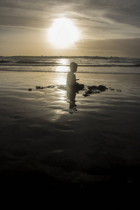 沙滩上玩耍的男孩的剪影，夕阳西下，在海中倒影