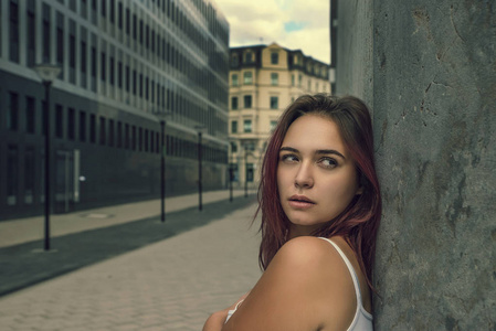 一位年轻美丽的女孩斜靠在一座城市街道大楼的墙上的肖像。