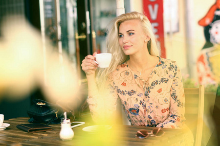 午休的金发女人坐在夏天的户外咖啡馆里，喝杯咖啡，近距离拍照