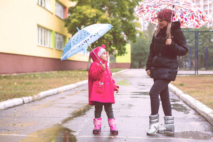 年轻漂亮的女人带着漂亮的小女儿带着雨伞走在公园里