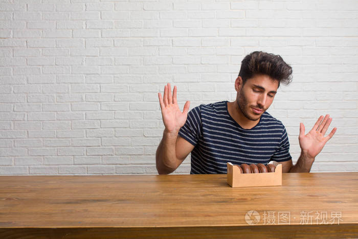 年轻英俊自然的男人坐在桌子上怀疑和耸肩的概念,优柔寡断和不安全感