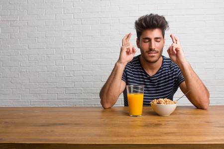 年轻英俊自然的男人坐在桌子上交叉手指,希望能为未来的项目感到幸运