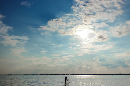 妈妈和孩子站在水里，面对湖面上美丽的日落。 母性爱家庭的概念。