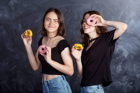 快乐漂亮的十几岁女孩和甜甜圈玩得很开心。 黑色背景上有甜甜圈的快乐女孩的肖像。 良好的情绪饮食观念。
