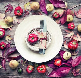 鲜红色的甜椒放在盘子里，秋叶餐具和木制背景的梨