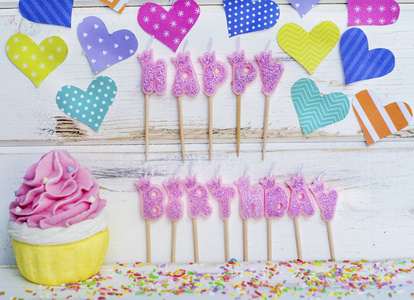 粉色生日快乐蜡烛蛋糕和白色木制背景上五颜六色的心