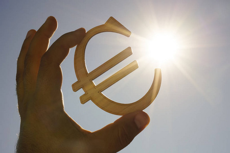 s hand holding  wooden Euro sign against blue  sky. 