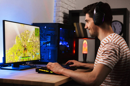 欧洲玩家的肖像，在电脑上玩电子游戏，戴着耳机，使用背光的彩色键盘