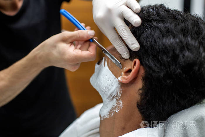 这个年轻人正在理发店里用一把直剃刀刮胡子