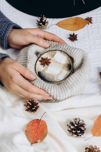 s hands hold a cup with hot coffee with marshmallows, scarf, coo