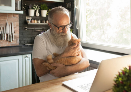 老人带着他的猫在笔记本电脑上工作，微笑着看着屏幕。
