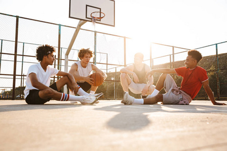 一群年轻的微笑的多民族男子篮球运动员在运动场上休息交谈