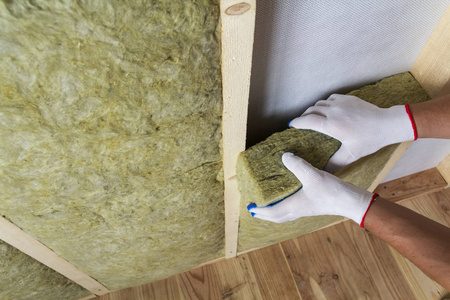 关闭工人手在白色手套绝缘岩棉绝缘工作人员在木制框架，为未来的墙壁冷屏障。 舒适温馨的家居经济建设和改造理念。