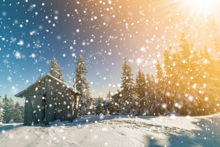 在五彩缤纷的蓝天和雪花背景下,山上白雪皑皑的木制牧人小屋在松树