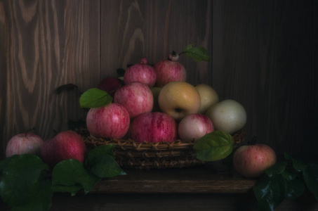 小柳条篮子，苹果放在木架上，靠在木墙上。 被柔和的环境光照亮。