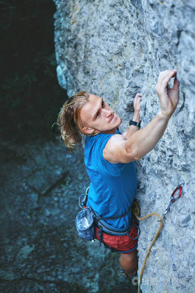 长头发的攀岩者顶部的年轻人攀岩者穿着鲜红色短裤攀
