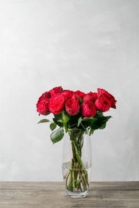 花瓶上的红玫瑰在木桌上。花园牡丹红钢琴